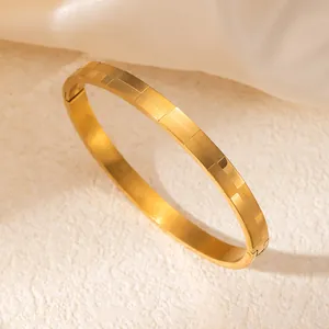 Detalle de brazalete de acero inoxidable dorado con textura de cuadros y cierre plegable