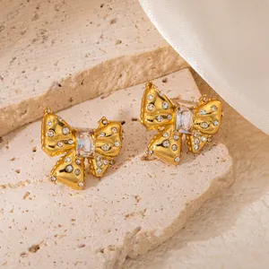 Gros plan de boucles d'oreilles nœud dorées avec strass brillants sur fond de pierre