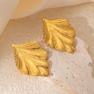Vista macro di orecchini a foglia placcati oro con texture venate su fondo in pietra