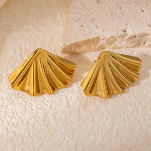 Dettaglio di orecchini dorati a forma di ventaglio su una base in pietra minimalista