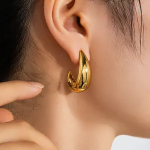 Gros plan d'un mannequin portant des boucles d'oreilles gouttes dorées polies en acier