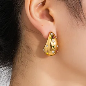 Gros plan de boucles d'oreilles gouttes dorées serties de zircons colorés sur un modèle