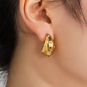 Gros plan de boucles d'oreilles goutte en or 18K avec zircons colorés portées à l'oreille