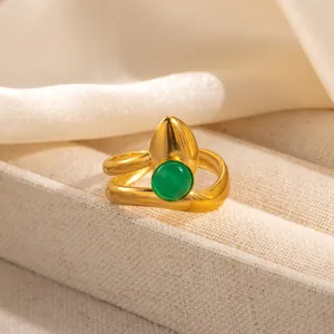 Detail of a gold wavy ring with a green round gemstone and pointed metallic element