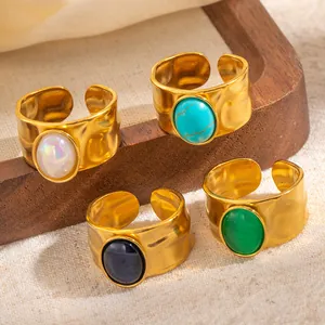 Detail van vier goudgehamerde open ringen met ovale edelstenen op houten voet