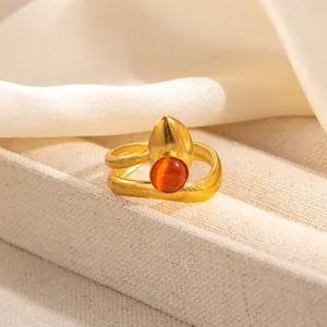 Detail of a layered gold ring with a teardrop charm and orange cat-eye gemstone