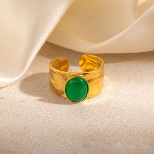 Detail van een gouden verstelbare ring met gehamerde textuur en groene edelsteen