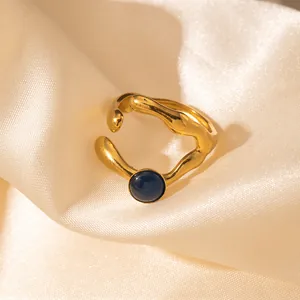 Dettaglio anello dorato ondulato con gemma blu scuro su sfondo di seta color champagne