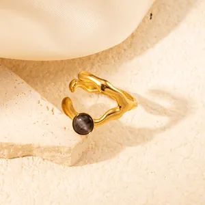 Dettaglio dell'anello dorato ondulato con gemma grigia su sfondo di seta color crema