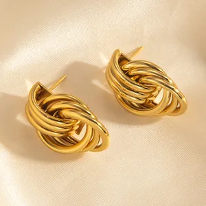 Detailed view of intertwined 18k gold rings earrings on soft silk fabric background