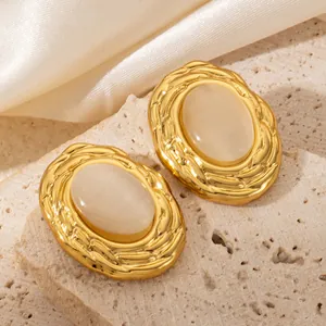 Detail view of 18K gold plated oval earrings with opalescent center on a marble surface