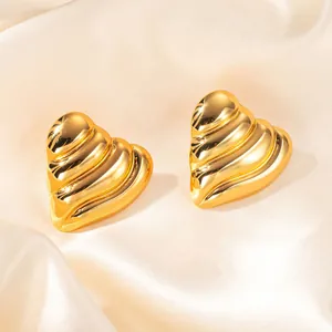 Dettaglio degli orecchini a cuore dorati con strisce su tessuto in seta beige