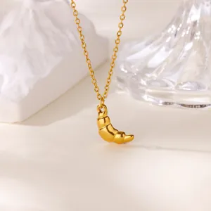 Detailed view of golden croissant pendant necklace on stone and glass backdrop