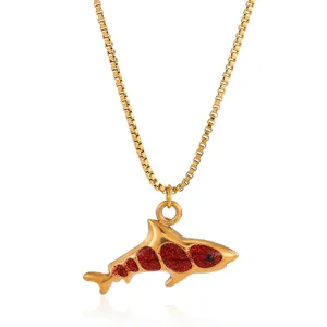 Detail of shark pendant necklace in gold finish with red glitter inlay on white background