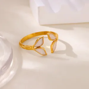 Macro detail of a gold open ring featuring four white floral enamel petals on a minimal prop