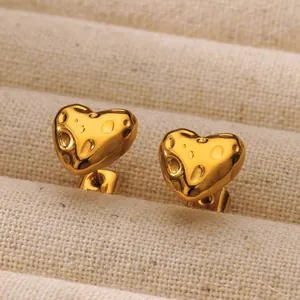 Detailed close-up of golden heart earrings with irregular hammered texture on jewelry tray
