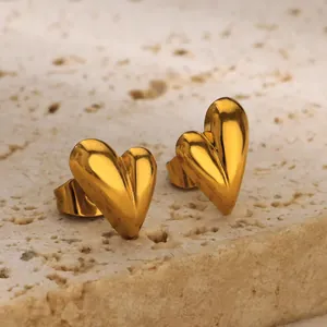 Close-up of golden heart earrings on a beige stone stand with polished metallic texture