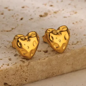 Macro shot of gold heart stud earrings with irregular hammered texture on stone base
