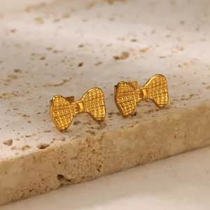 Macro detail of golden bow earrings with checkered texture on a light stone base