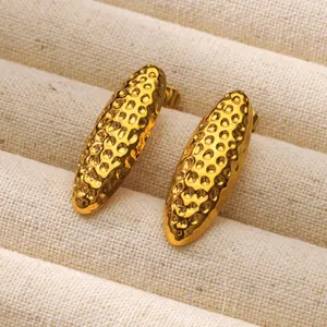 Vista macro de pendientes dorados con textura martillada sobre bandeja de joyería