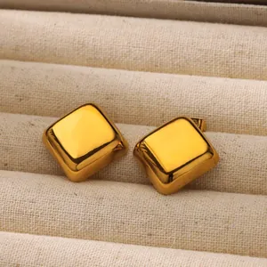 Primer plano de aretes cuadrados de oro pulido en un estuche de joyería color beige
