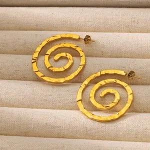 Primer plano de pendientes de espiral dorados con textura martillada en bandeja beige