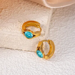 Polished gold hoop earrings with a vibrant sky blue round zircon stone on stone background