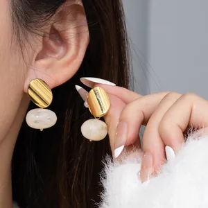 Boucles d'oreilles ovales dorées avec pendentif en pierre marbrée portées sur modèle
