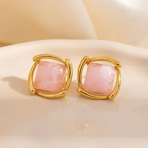 Boucles d'oreilles carrées dorées avec pierres marbrées roses sur un plateau en céramique