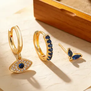 Dettaglio degli orecchini dorati con ciondoli a stella e occhio in zircone blu