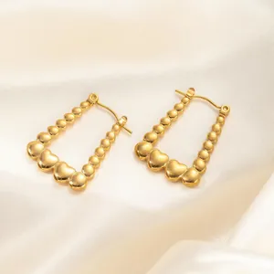 Elegant gold titanium steel hoop earrings with bead and heart charms on silk background