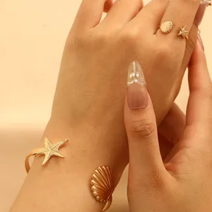 Primer plano de un brazalete dorado con estrella de mar y concha con anillo a juego
