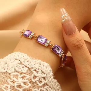 Dettaglio di bracciale dorato con gemme rettangolari viola e zirconi bianchi su raso