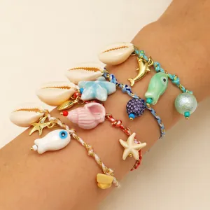 Close-up of bohemian ocean-style braided bracelets with shell and ceramic fish charms