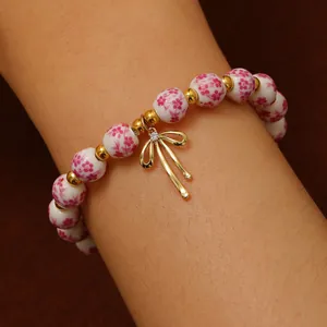 Dettaglio del bracciale con perline di ceramica e ciondolo a fiocco dorato sul polso