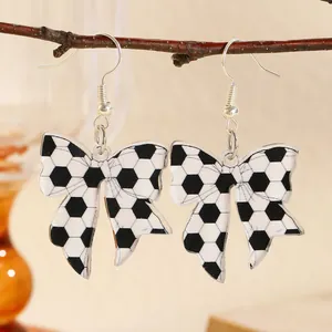 Detailed view of soccer pattern bow earrings hanging on a natural wooden branch