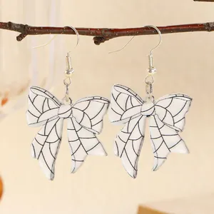 Detail of white bow earrings with black grid pattern hanging on a natural branch