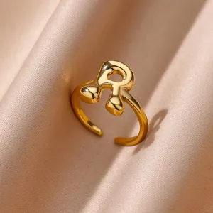 Detail van een 18K vergulde bubble letter R ring op elegante champagne satijnen stof