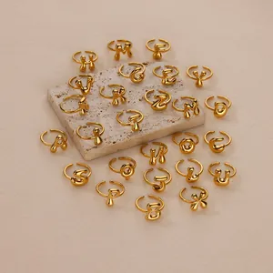 Set van 26 vergulde 18K bubble letter open ringen gepresenteerd op een beige stenen houder