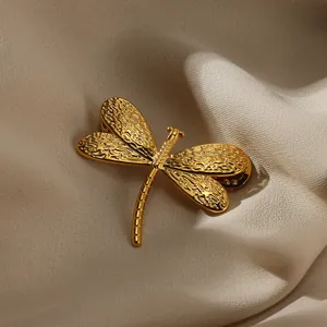 Vintage golden dragonfly brooch with hammered wings on elegant beige silk fabric background