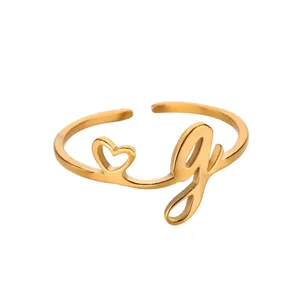 Détail d'une bague dorée en acier inoxydable avec cœur ajouré et breloque lettre G