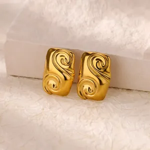 Macro shot of gold camellia earrings with spiral relief texture on a stone prop