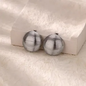 Detail of silver stud earrings with horizontal striped texture on a stone background