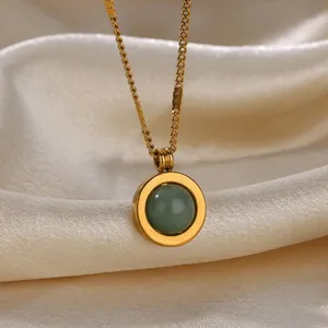 Macro shot of gold oval pendant with green stone on ivory silk background fabric