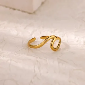 Detail of a wavy 18K gold plated stainless steel ring on a minimalist stone background