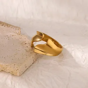 Close-up of golden irregular wavy ring with matte finish on a beige textured stone base