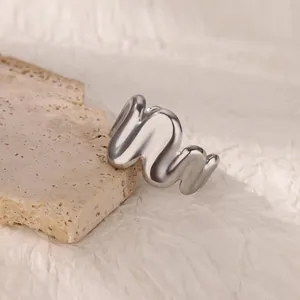 Close-up of polished silver fluid wave ring on natural stone against textured paper