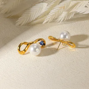 Gros plan sur les boucles d'oreilles nœud en plaqué or 18K avec perle et pierre de cœur bleue