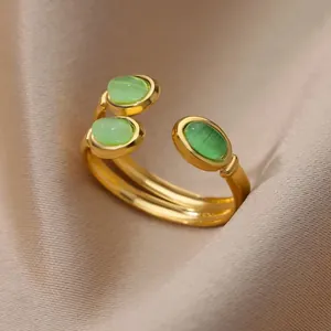 Close-up of 18K gold-plated open ring with three green oval stones on satin fabric
