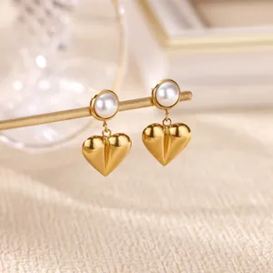 Vue détaillée des boucles d'oreilles cœur dorées avec perles sur un support minimaliste